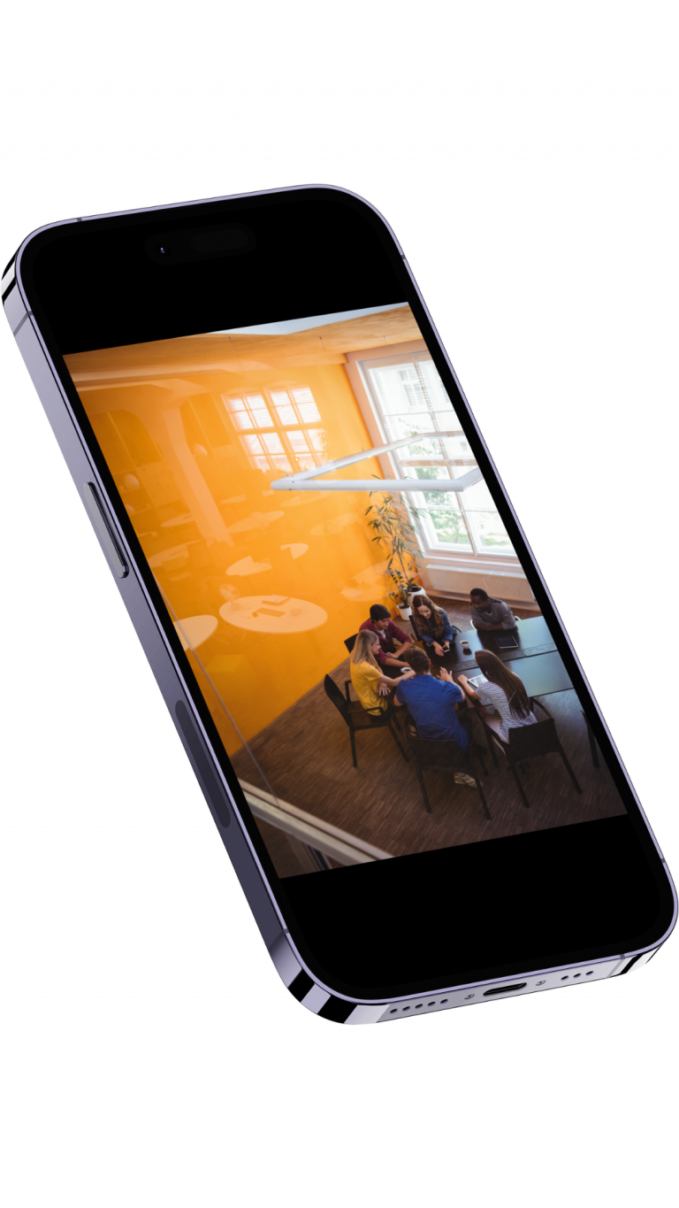Six people seated around a conference table in a bright orange meeting room, shown on a tilted smartphone screen.